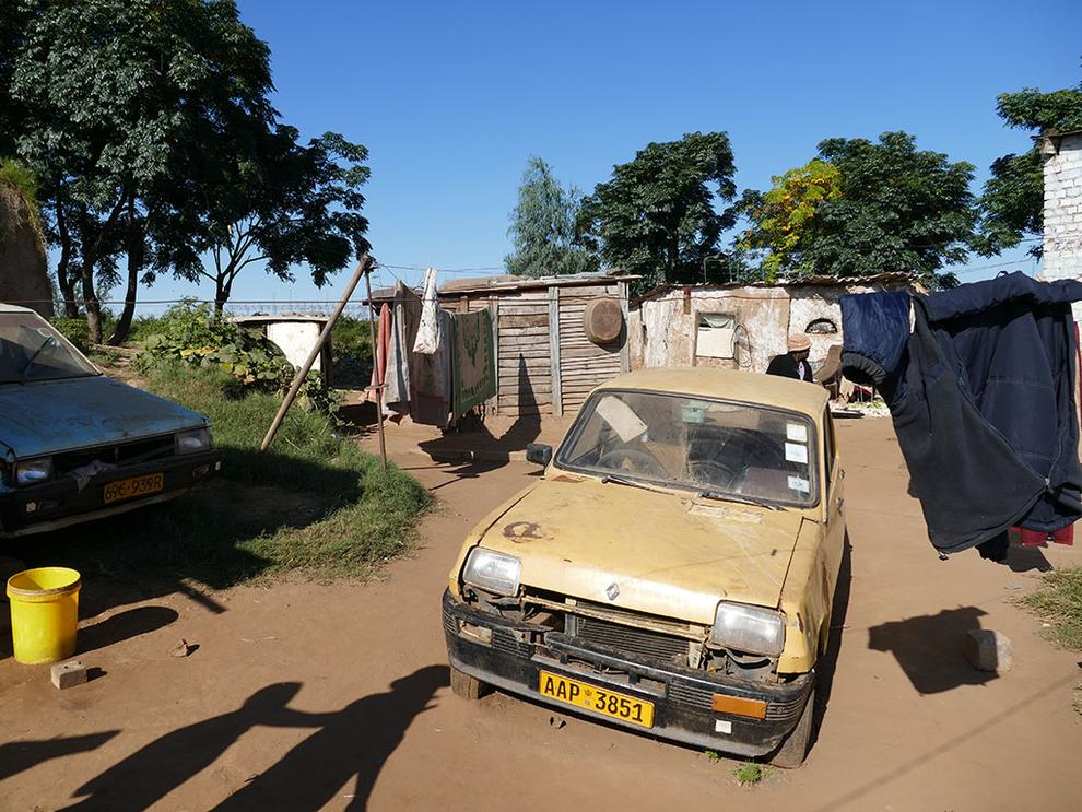 Zwei kaputte Autos und eine Hütte in Simbabwe davor eine Wäscheleine. 