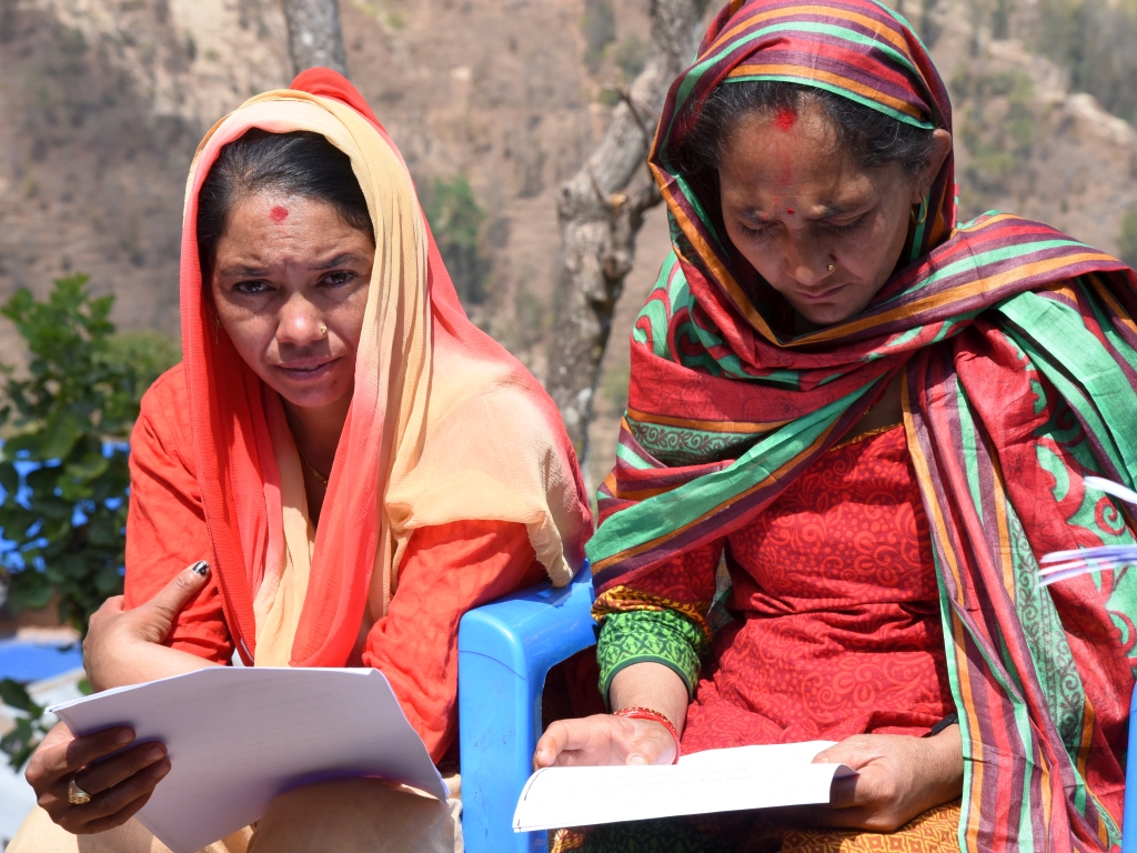 zwei nepalische Frauen mit Schals um den Kopf lesen einen Ausdruck